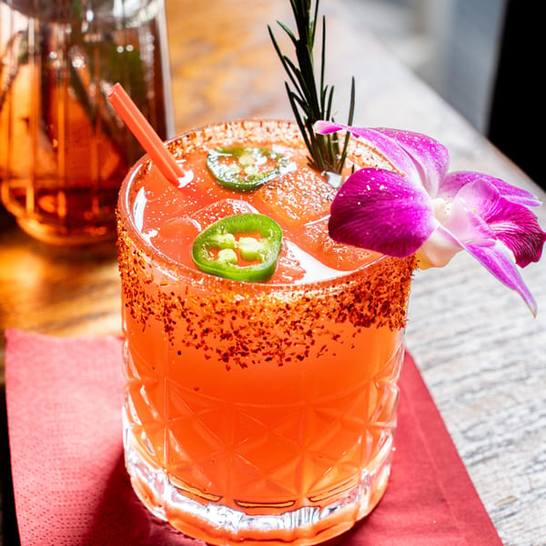 Nur Thai cocktail with chili-salted rim, jalapeño slices, rosemary, and a purple orchid garnish.