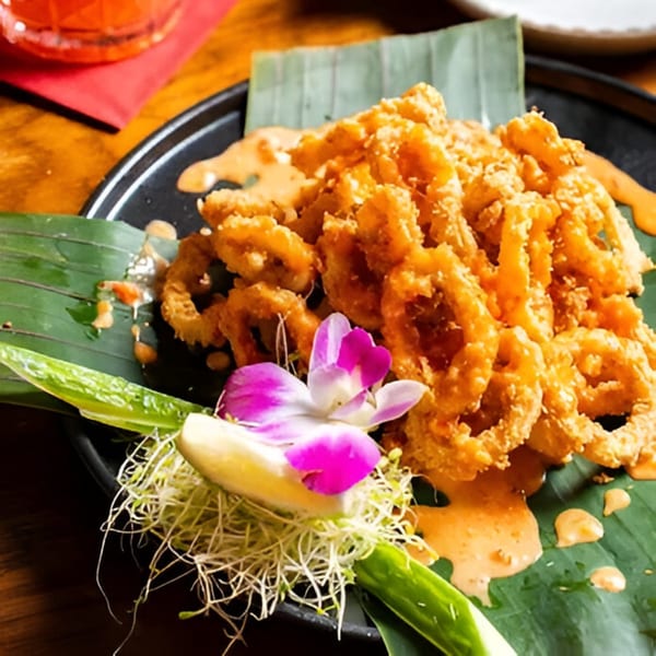 Crispy fried calamari rings with sauce, garnished with an orchid and sprouts on a banana leaf.