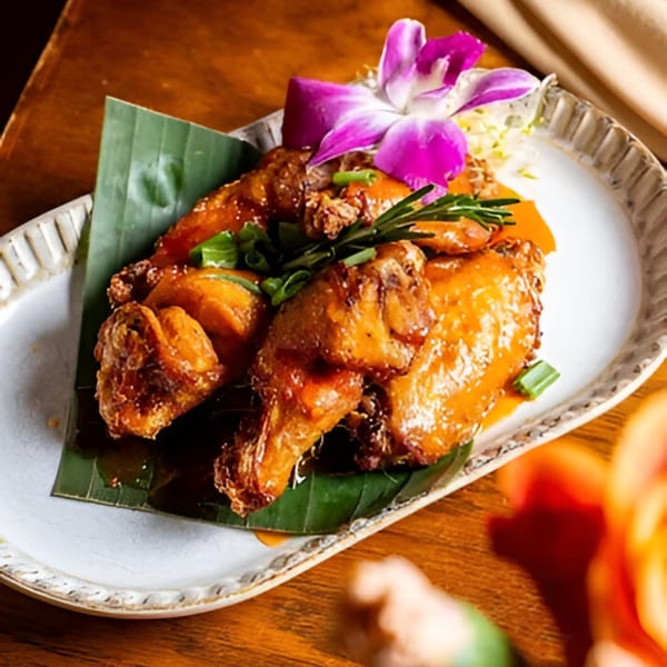 Nur Thai's crispy chicken wings with orange sauce, green onions, and a purple orchid garnish.