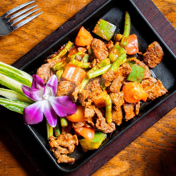 Nur Thai's spicy beef stir-fry with green beans and bell peppers, garnished with an orchid.