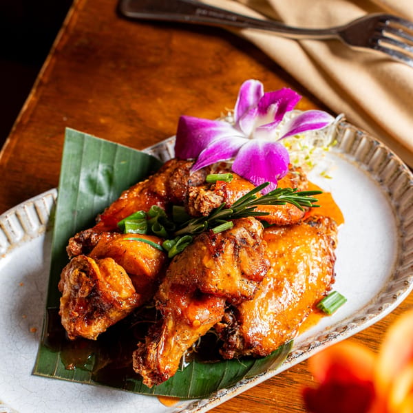 Nur Thai's glazed chicken wings on a banana leaf, garnished with green onions and an orchid.