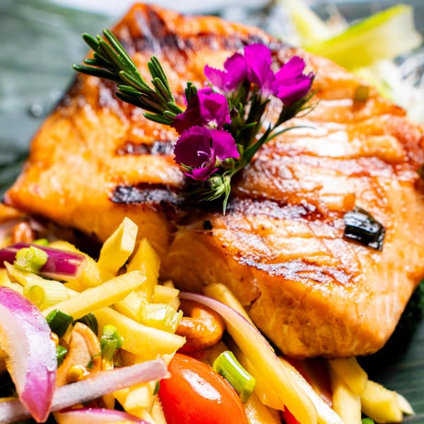 Grilled salmon with rosemary and purple flowers, served with a colorful mango salad.