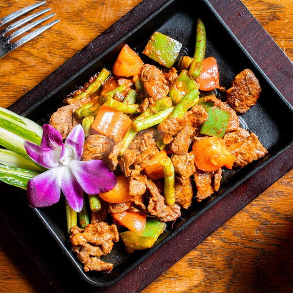 Sizzling Thai beef with green beans and bell peppers, garnished with a purple orchid.