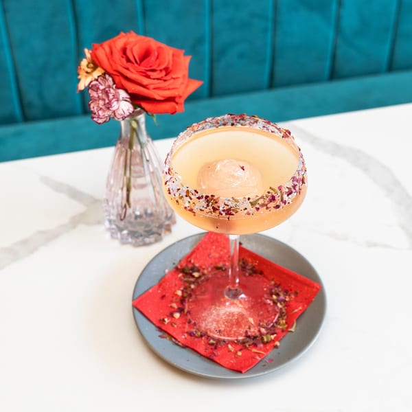 A Thai cocktail with a lychee garnish and a sugar-rimmed glass, next to a vase of red roses.