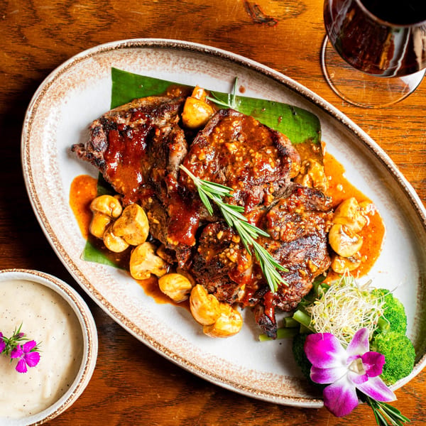 Nur Thai's grilled steak with mushrooms, broccoli, sprouts, and a purple orchid garnish.