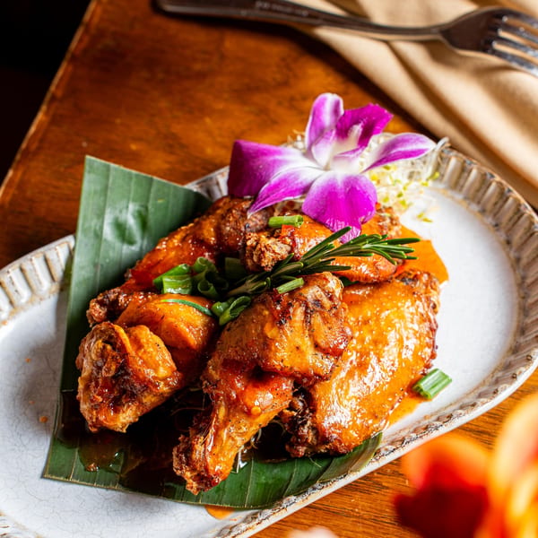 Nur Thai's crispy chicken wings, garnished with rosemary, green onions, and an orchid.