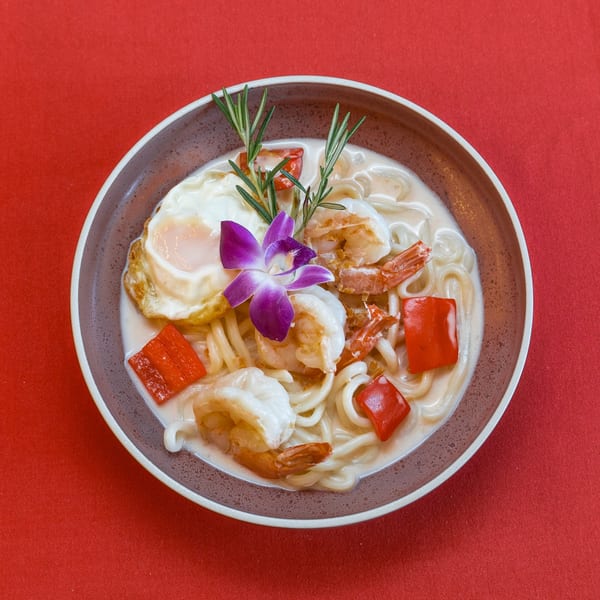 Nur Thai's creamy noodle dish with shrimp, red peppers, fried egg, rosemary, and an orchid.