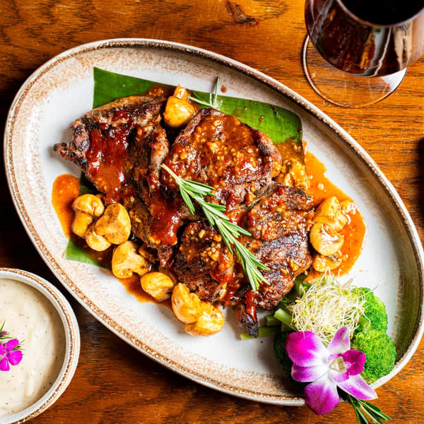 Nur Thai's steak with mushrooms, broccoli, and a purple orchid on a banana leaf.